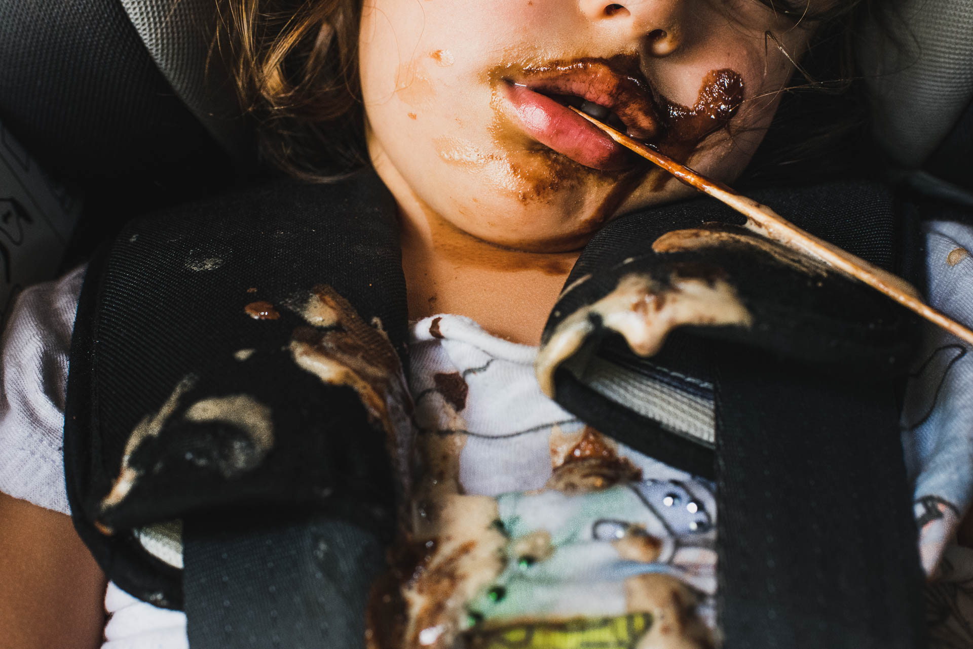 Kind eingeschlafen im Kindersitz mit Glacestängel im Mund und Glaceresten auf der Kleidung